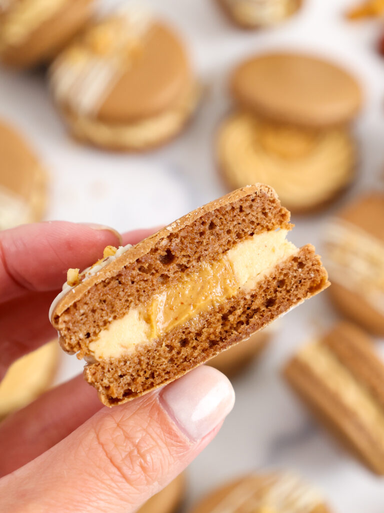 image of a chocolate peanut butter macaron that's been cut open to show its full shells and delicious honey roasted peanut butter center and buttercream filling
