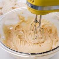 image of spiced cream. cheese frosting that's being made in a bowl with a hand mixer