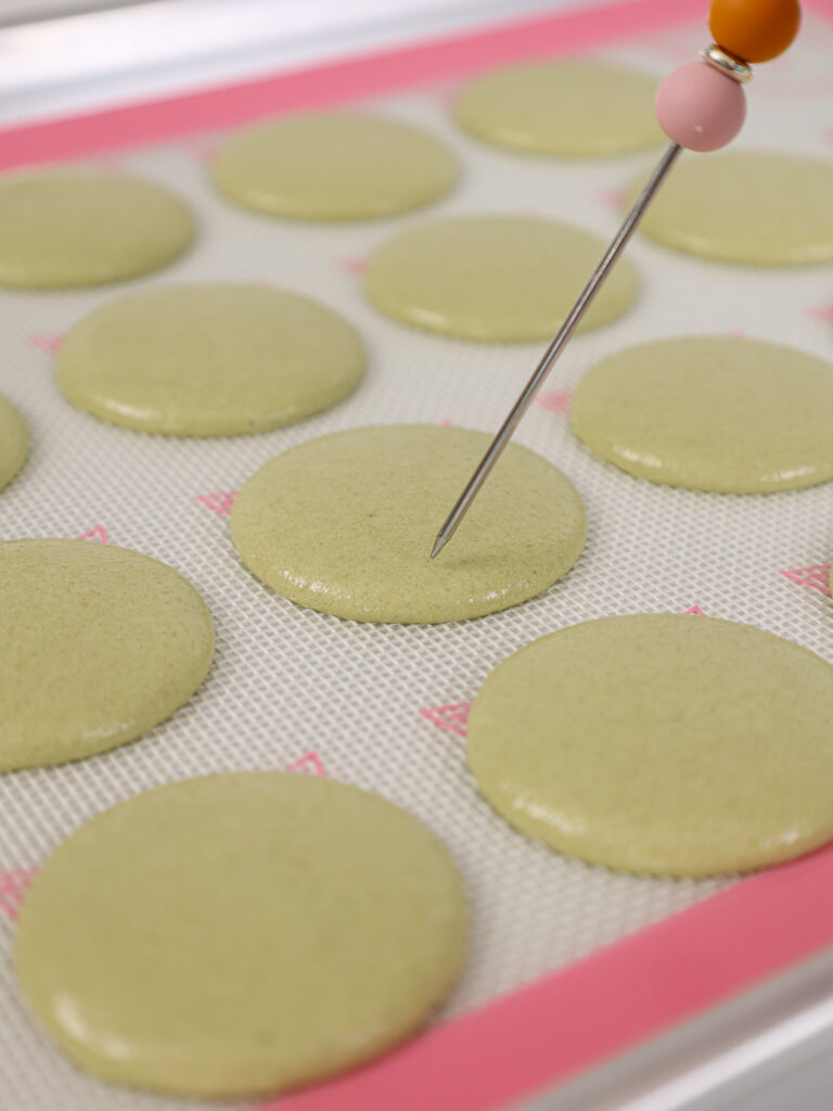 image of matcha macaron shells that have been piped and are having any bubbles be popped with a scribe