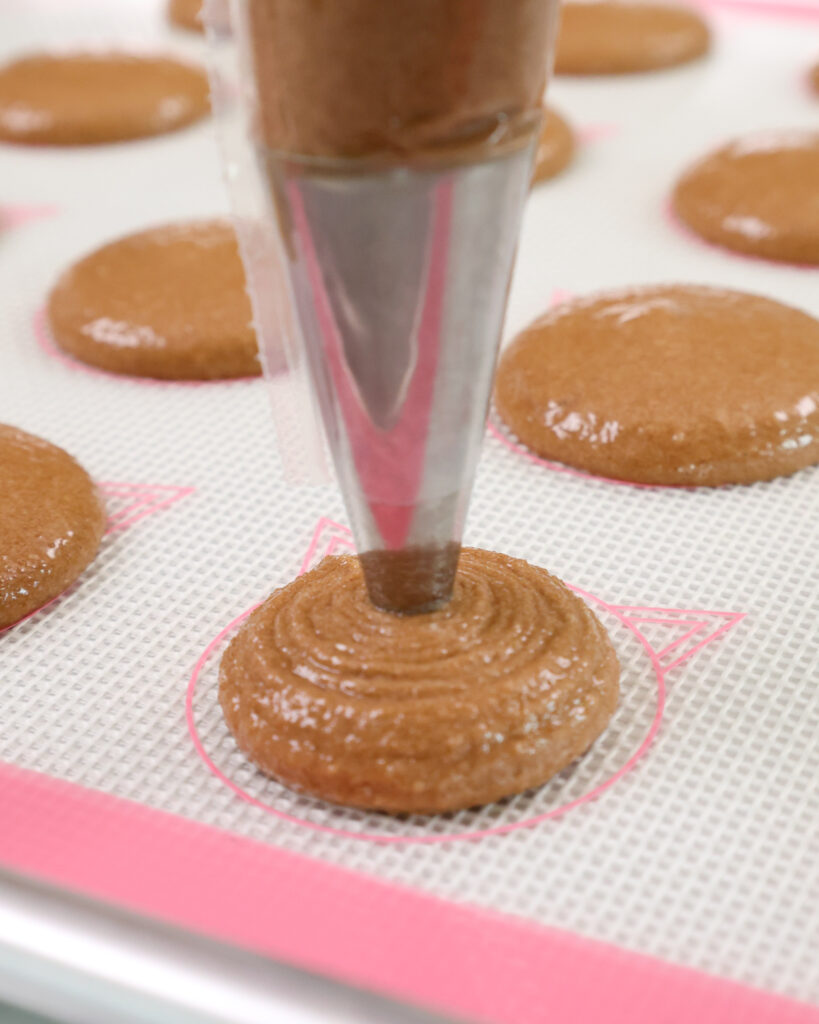image of chocolate macaron shells being piped onto a silpat mat