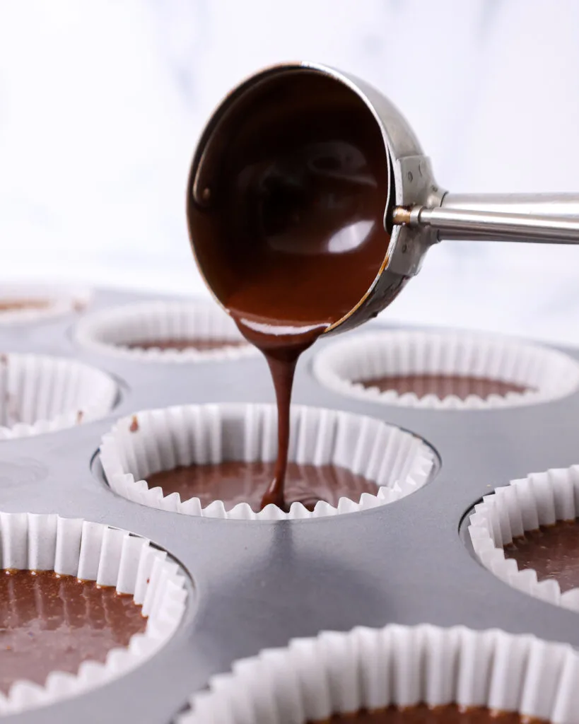 image of chocolate cupcake batter being poured into a cupcake liner with a cookie scoop