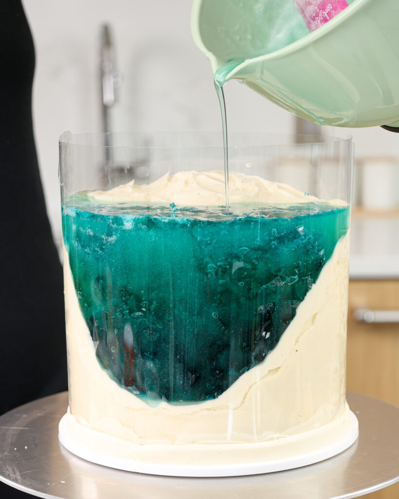 pouring liquid gelatin into an acetate sheet lined cake to make a jelly beach cake