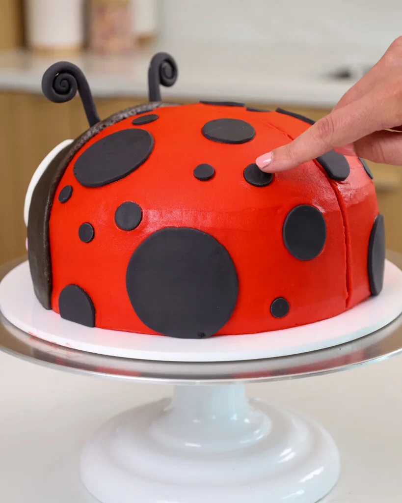 image of black fondant spots being pressed into buttercream on a lady bug birthday cake