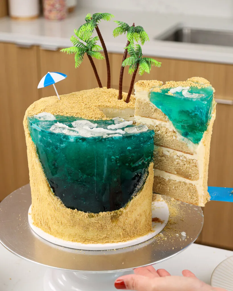 image of a slice of cake being pulled out of a cake that's been decorated to look like a tropical island