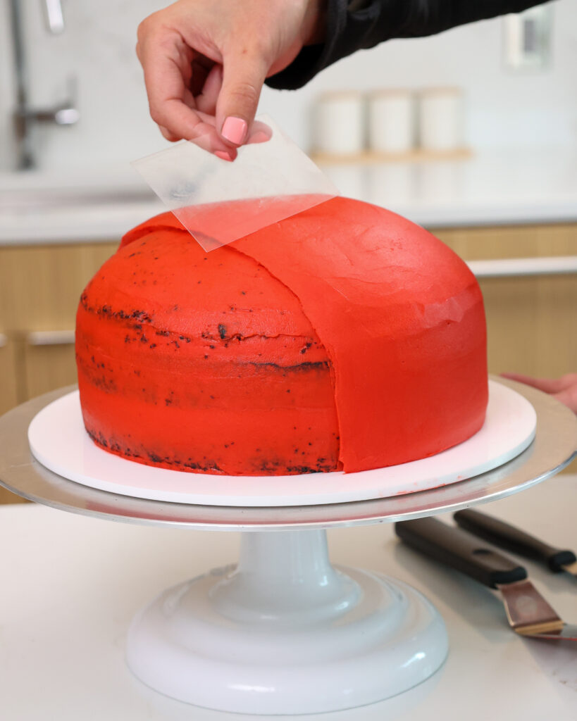 image of red buttercream being smoothed onto a rounded cake