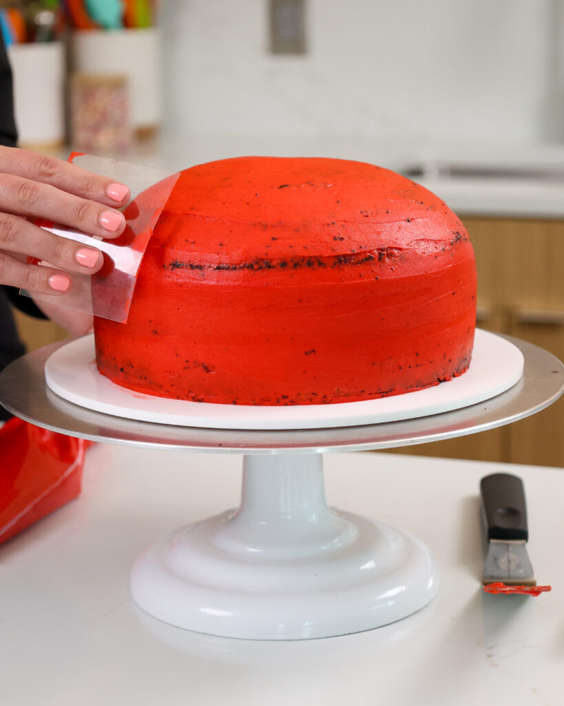 image of red buttercream being smoothed onto a domed cake as a crumb coat