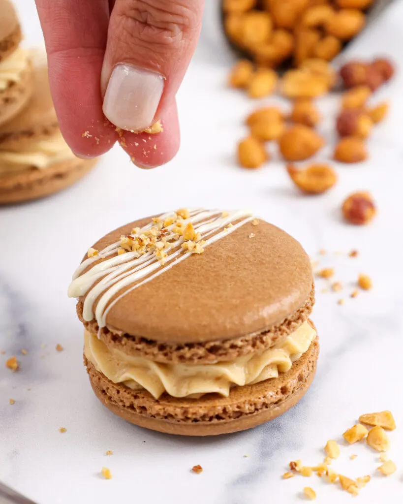 image of chopped up honey roasted peanuts being sprinkled on top of a peanut butter macaron as a garnish