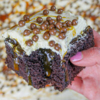 image of a chocolate caramel poke cake slice being held up to show it's caramel filling