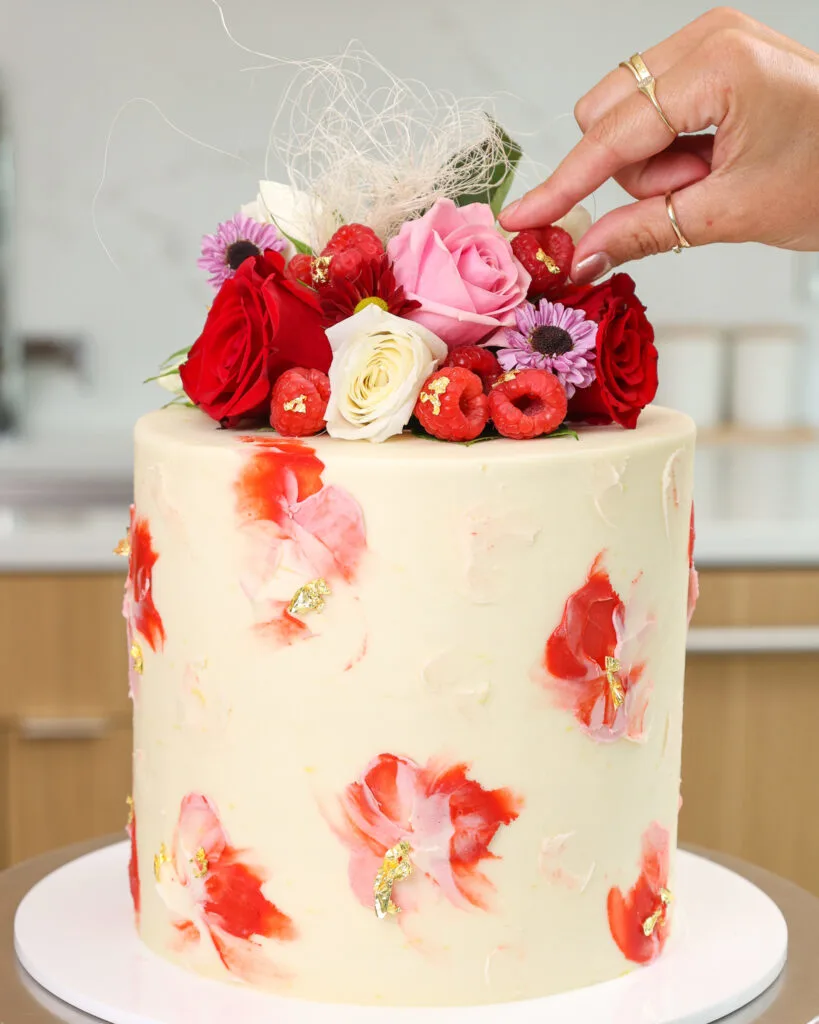 image of a beautiful white chocolate raspberry cake that's been topped with fresh flowers and berries for decoration