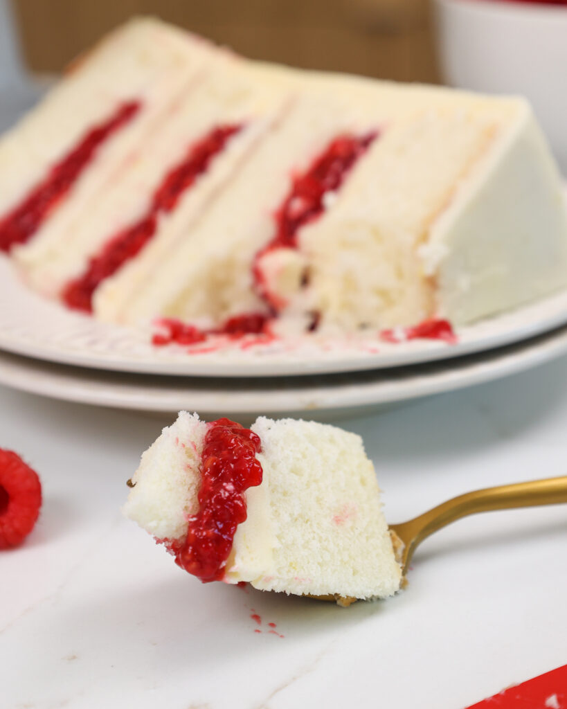 image of a white chocolate raspberry cake that is made with fluffy vanilla cake layers, tart raspberry cake filling, and white chocolate buttercream frosting