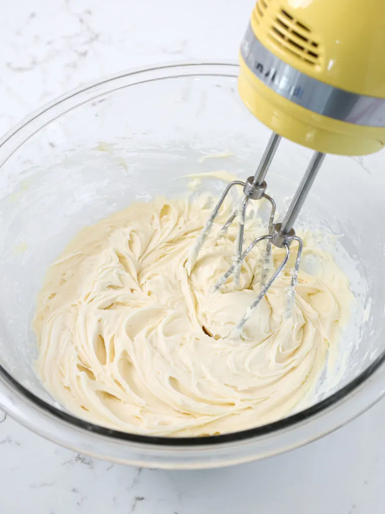 image of almond frosting being mixed in a glass bowl with a hand mixer