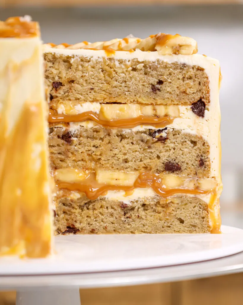 image of a banoffee cake that's been cut open to show its cross section of moist banana cake layers, toffee filling, banana slices and whipped vanilla buttercream