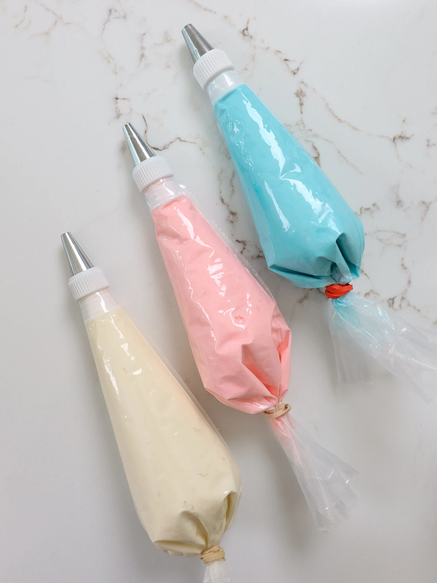 image of three piping bags filled with light pink, light blue, and white buttercream frosting