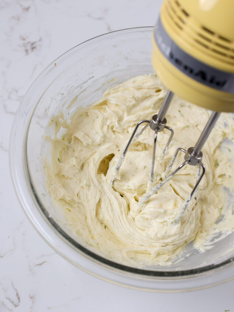 image of lime buttercream being mixed in a glass bowl with a hand mixer