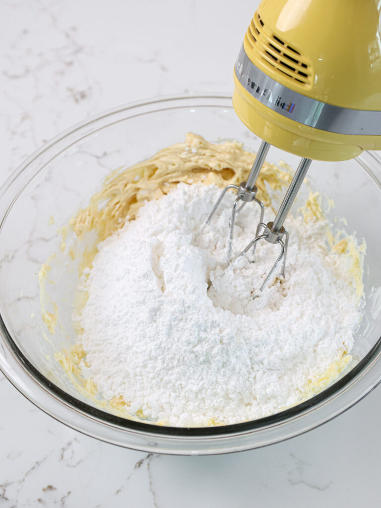 image of powdered sugar being mixed into butter and cream cheese to make homemade almond buttercream