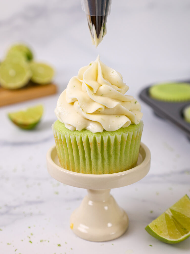 image of lime buttercream being piped on top of a lime cupcake