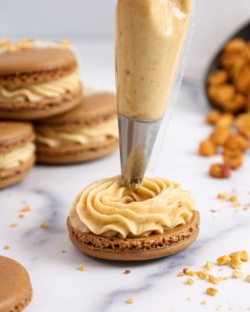 image of peanut butter buttercream being piped onto a chocolate macaron