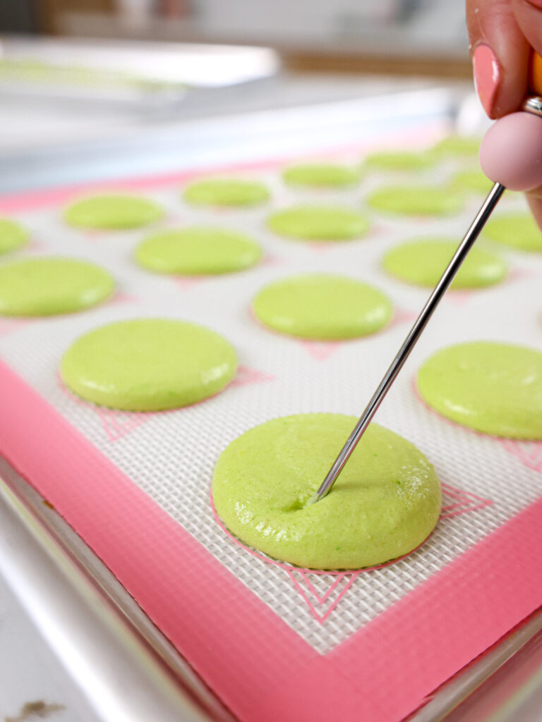 image of green macaron shells having their bubbles popped with a scribe
