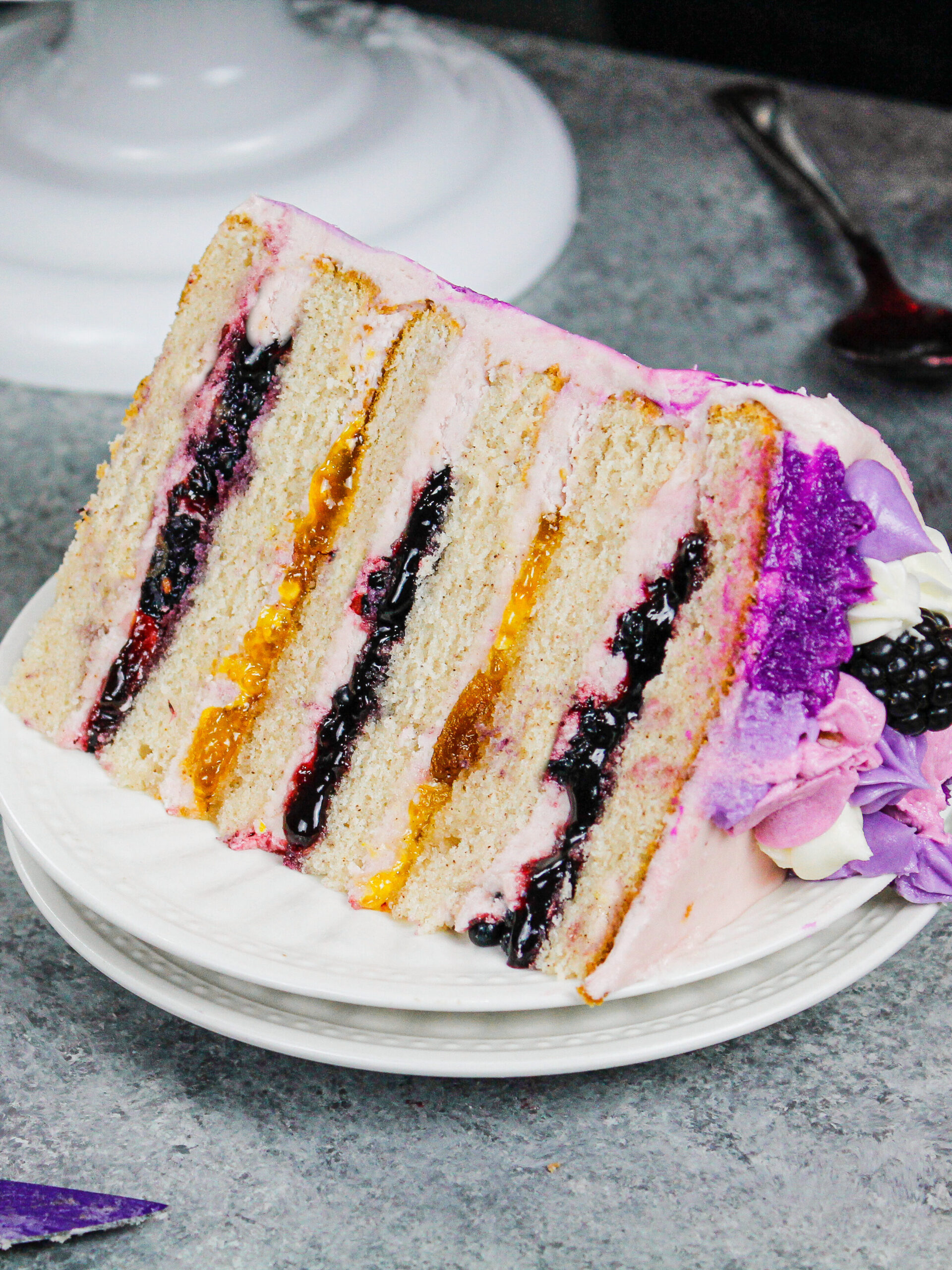image of a slice of blackberry layer cake being assembled with cinnamon cake layers, blackberry jam, fresh blackberries, and blackberry peach buttercream