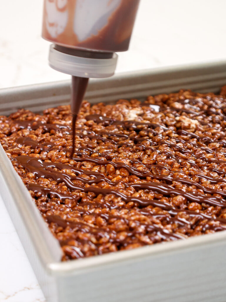 image of chocolate ganache being drizzled over a batch of chocolate rice krispie treats