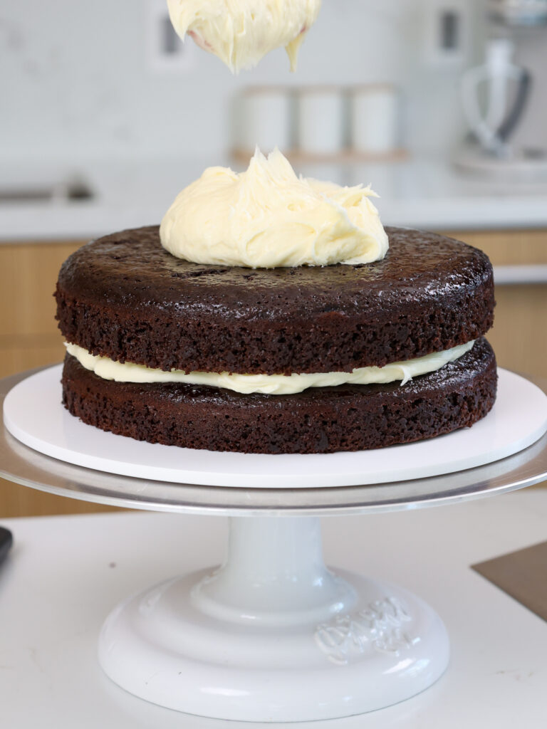 image of cream cheese frosting being spread between chocolate cake layers