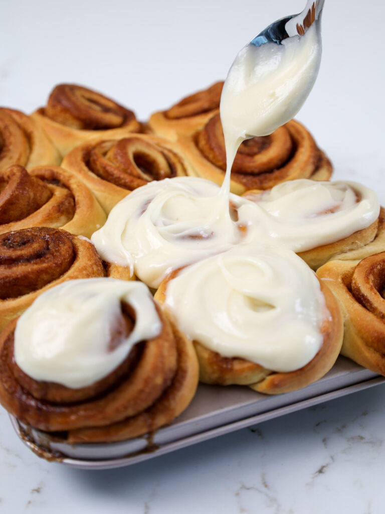image of a mini cinnamon roll being frosted with cream cheese frosting