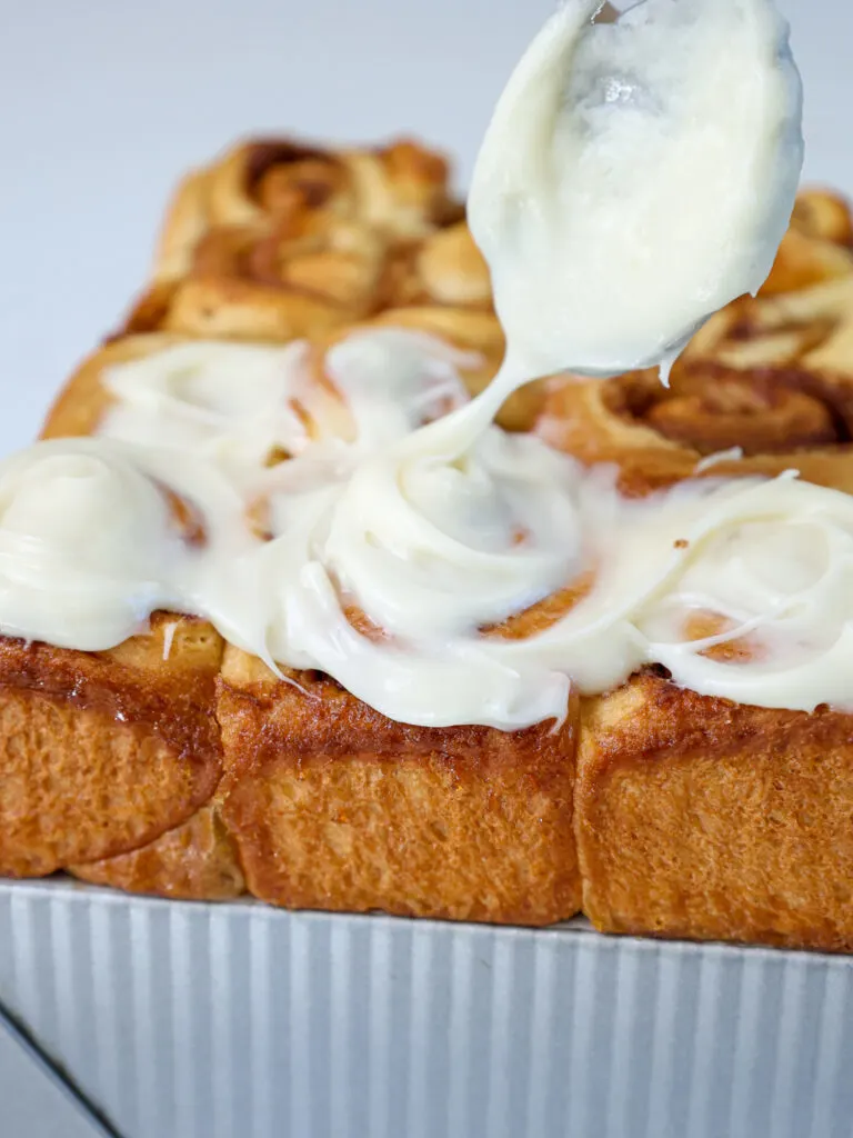 image of a mini cinnamon roll being frosted with cream cheese frosting