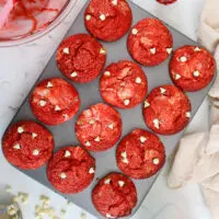 image of red velvet muffins that have been swirled with cream cheese filling and topped with white chocolate chips and crunch sanding sugar