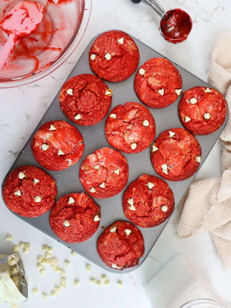 image of red velvet muffins that have been swirled with cream cheese filling and topped with white chocolate chips and crunch sanding sugar
