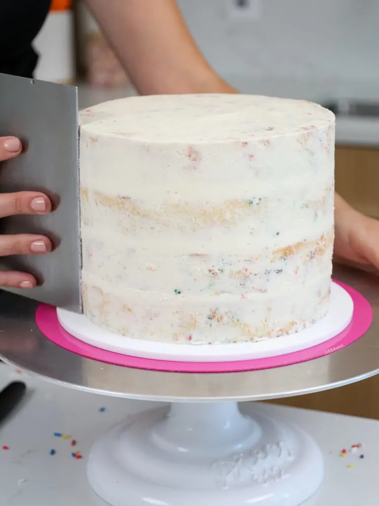 image of a funfetti cake being crumb coated and smoothed with a bench scraper