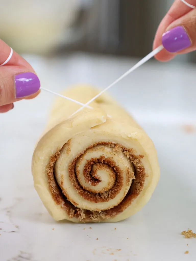 image of a log of cinnamon roll dough being cut to make mini cinnamon rolls
