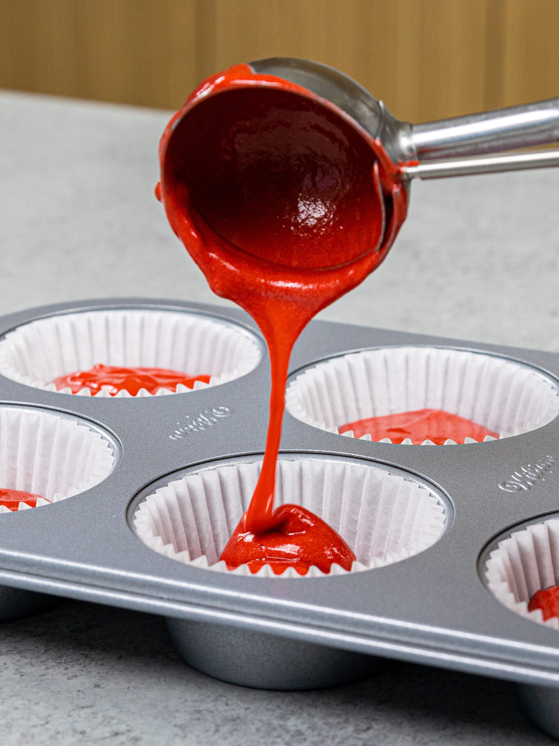image of red velvet cupcakes being scooped into cupcake liners