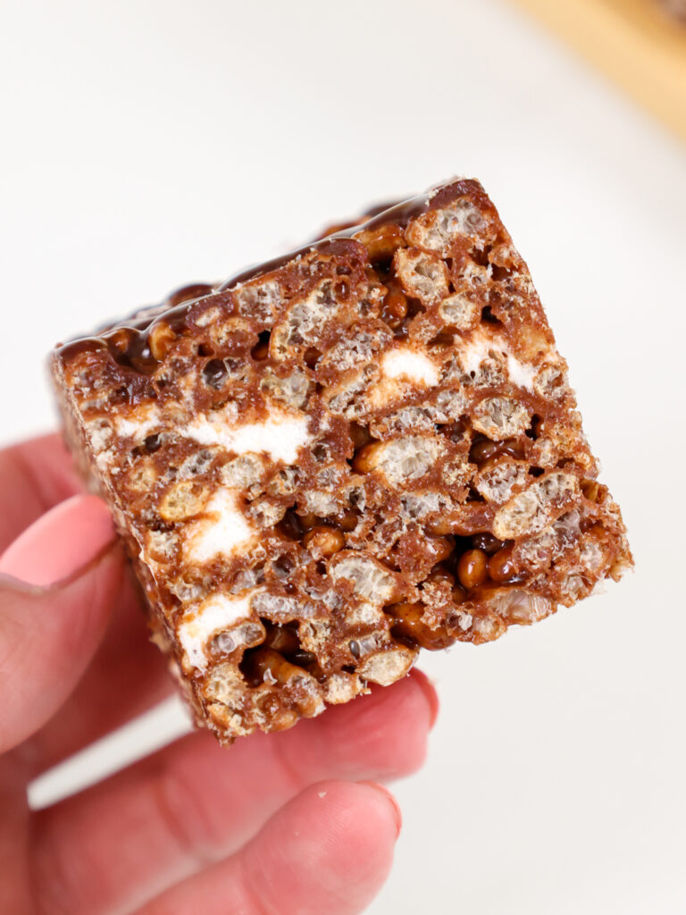 image of a chocolate rice krispie treat being held up to show it's chewy texture