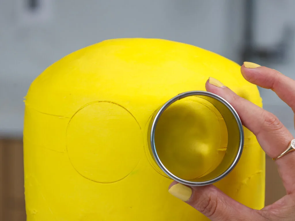 image of a circle cutter being used to map out where to pipe the details on a buttercream minions cake