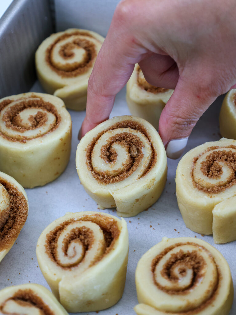 image of a mini cinnamon roll being placed in a baking pan to proof