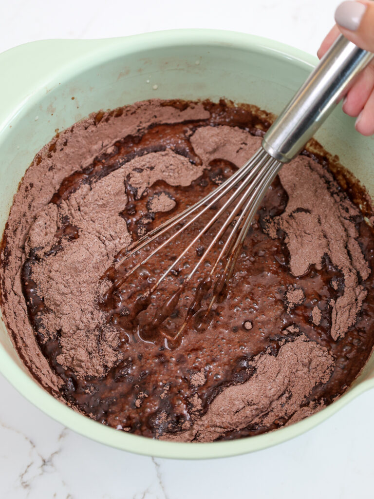 image of chocolate cake batter being made with a whisk in a green bowl