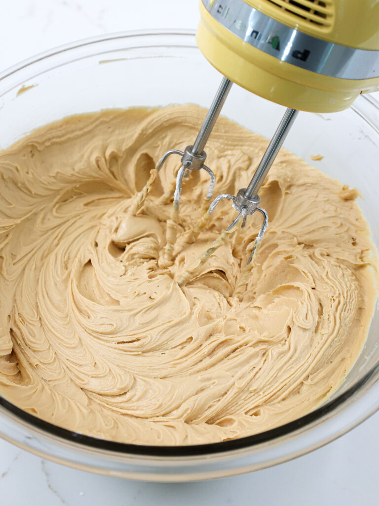 image of peanut butter cream cheese frosting that's being mixed with a yellow hand mixer