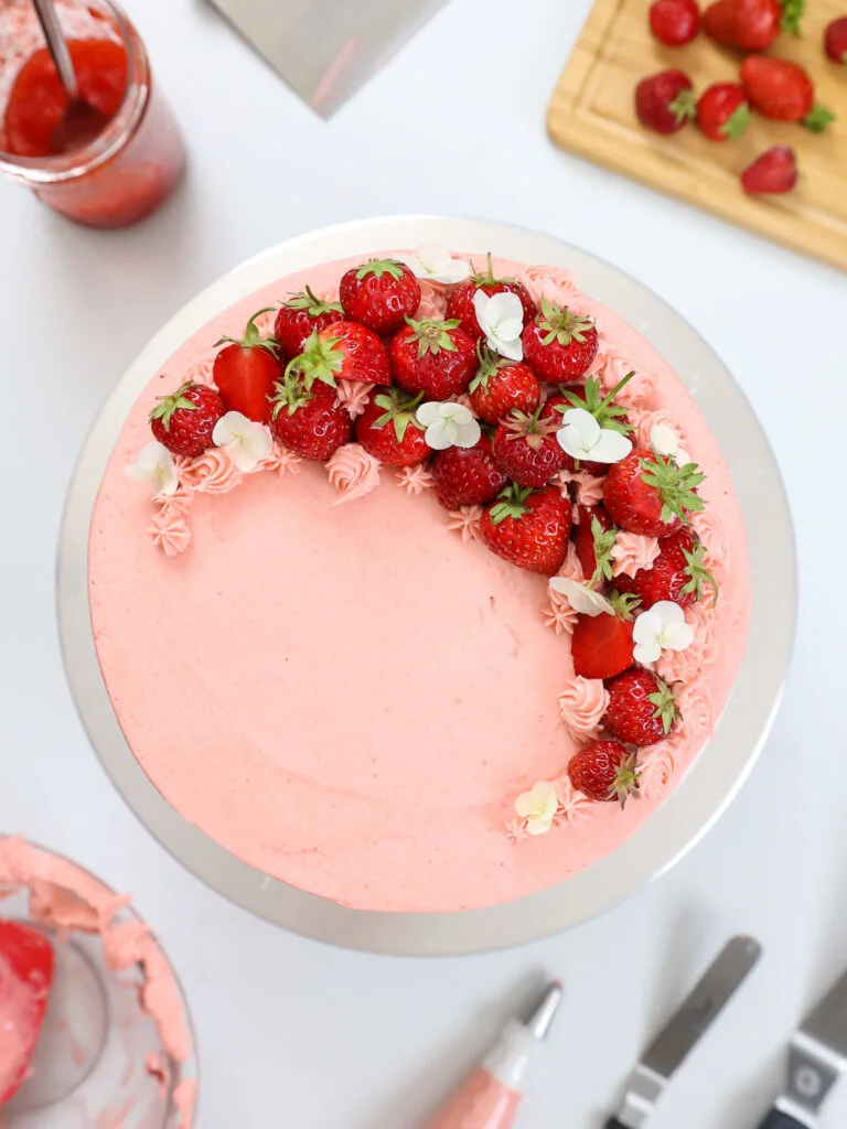 image of a strawberry cake that's been decorated with small strawberries and frosting dollops from an overhead vantage overhead 