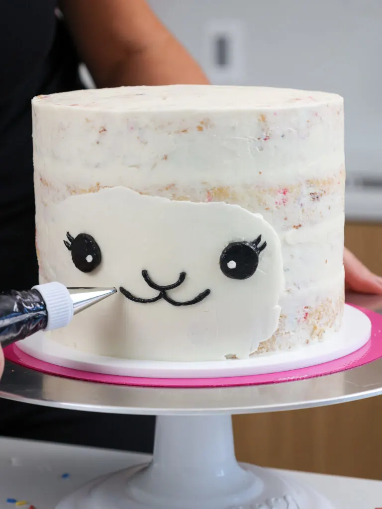 image of black buttercream being piped onto a llama cake to make its facial features