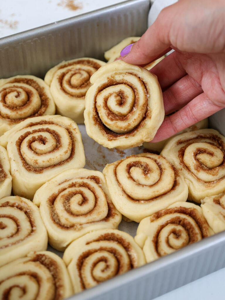 image of a mini cinnamon roll being placed inside a baking pan to be proofed