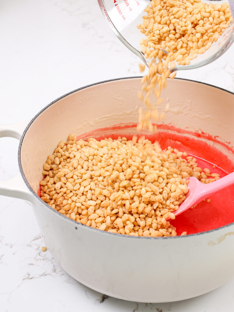 image of puffed rice cereal being poured into a large pot of melted strawberry marshmallows