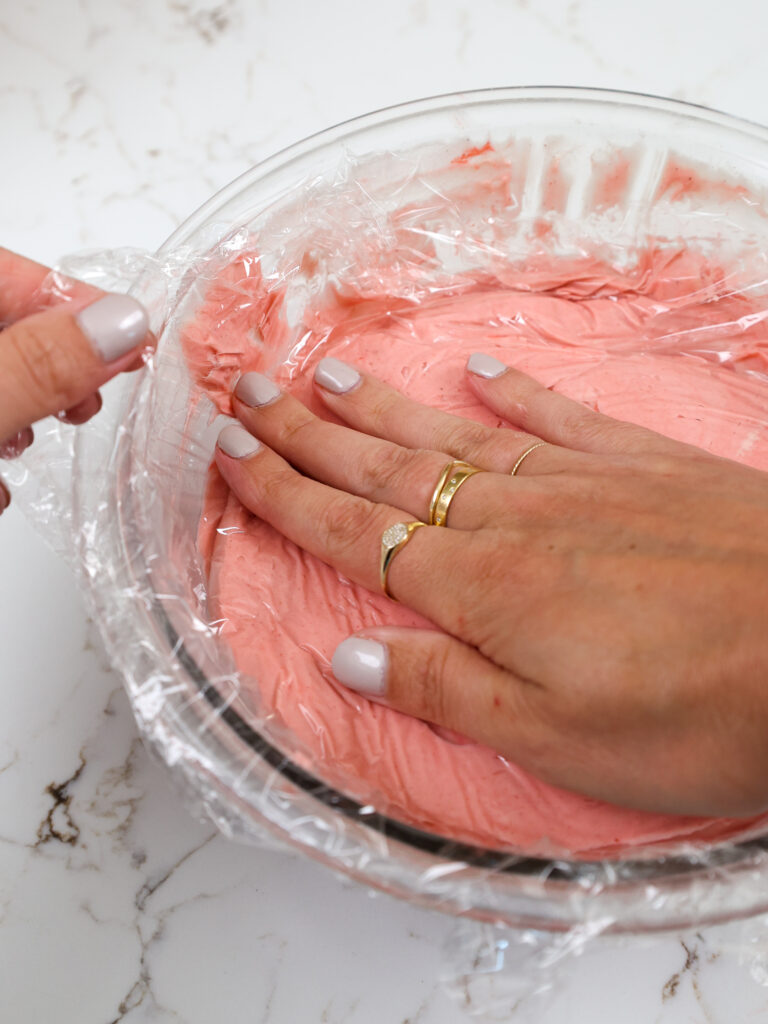 image of a bowl of strawberry mousse being covered with plastic wrap before being stored in the fridge