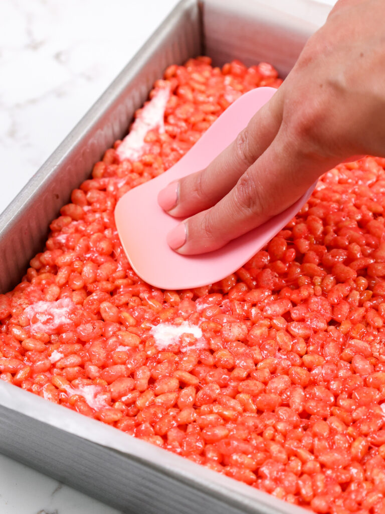 image of warm strawberry rice krispie treats being pressed into a square pan