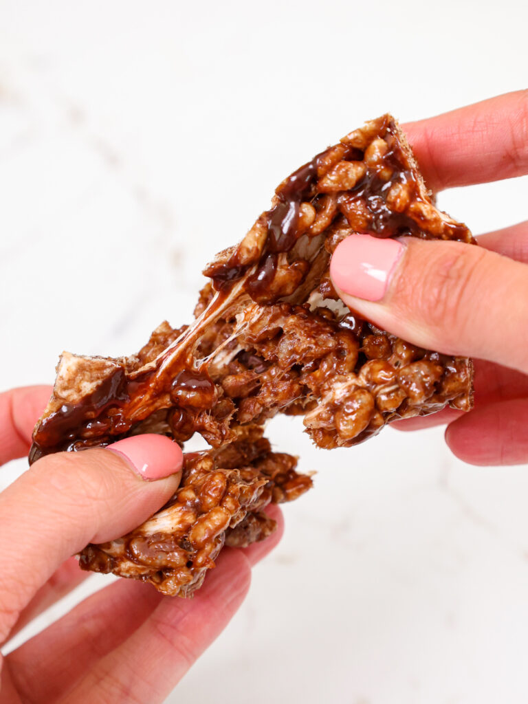 image of a chocolate rice krispie treat being pulled apart to show how gooey and delicious it is