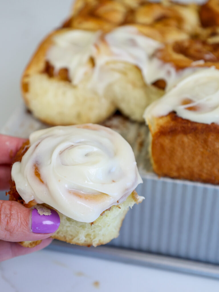 image of a mini cinnamon roll that's been frosted with cream cheese frosting and pulled apart from the rest