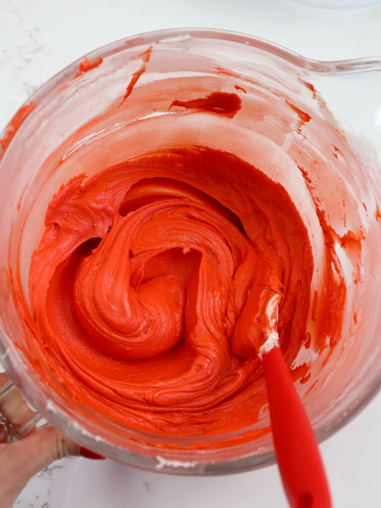 image of red buttercream frosting that's been made in a glass mixing bowl with red gel food coloring