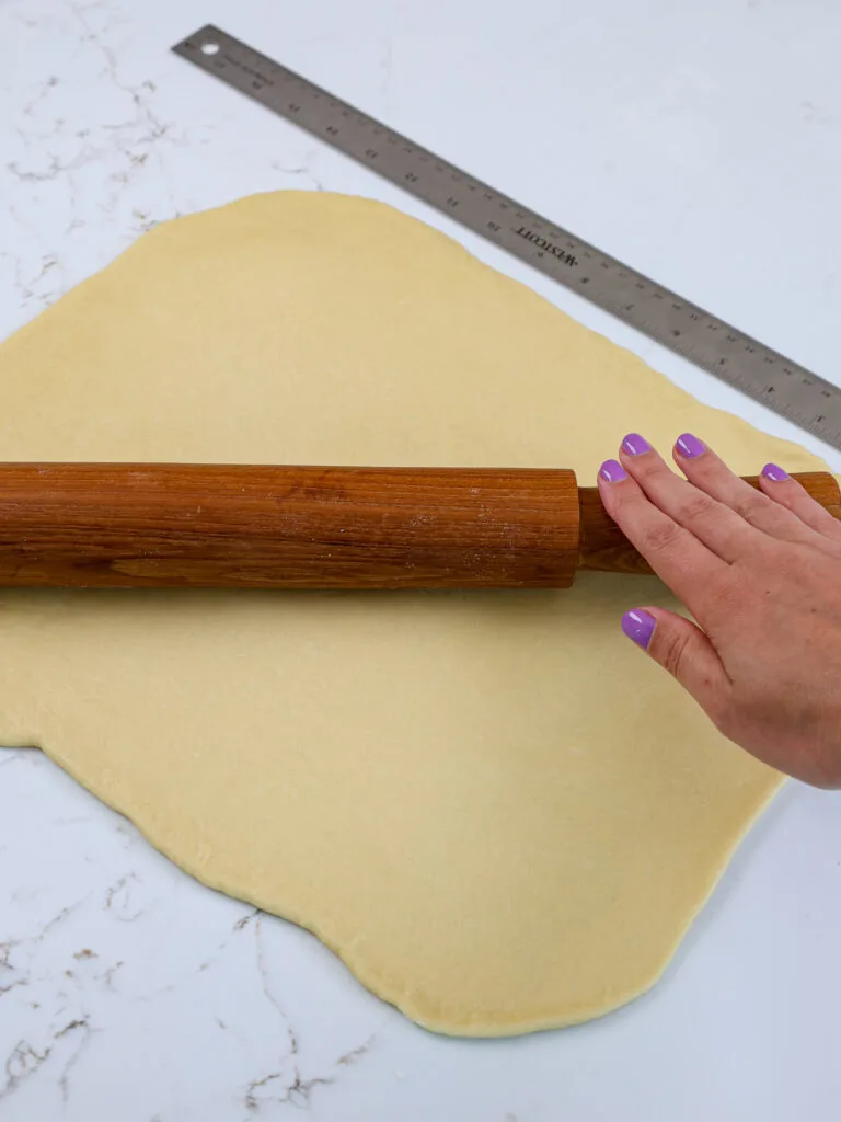 image of cinnamon roll dough being rolled out with a rolling pin