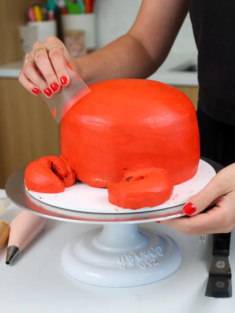 image of a crab birthday cake being frosted with red buttercream frosting