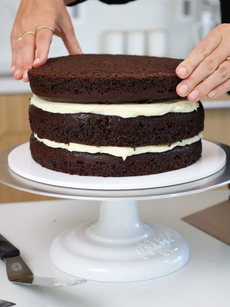 image of chocolate cake layers being stacked and filled with cream cheese frosting 
