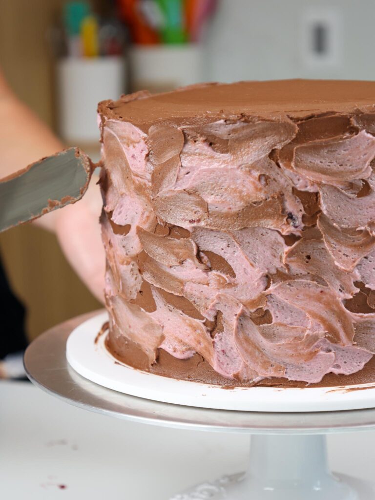 image of chocolate and blackberry buttercream being used to decorate the side of a chocolate blackberry cake